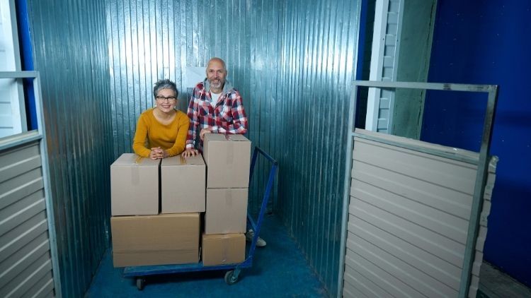 Two people standing with stacked moving boxes inside a storage unit. Two people standing with stacked moving boxes inside a storage unit.