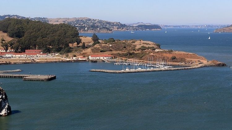 A view of a marina with small boats docked along the shoreline of San Francisco Bay, surrounded by hills and calm blue water with a few sailboats in the distance. A view of a marina with small boats docked along the shoreline of San Francisco Bay, surrounded by hills and calm blue water with a few sailboats in the distance.