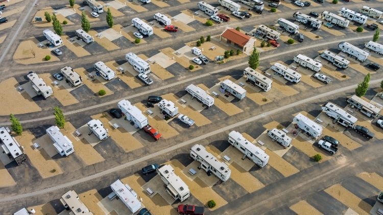 Aerial view of an organized RV park with rows of parked recreational vehicles, cars, and small trees along paved roads and gravel lots. Aerial view of an organized RV park with rows of parked recreational vehicles, cars, and small trees along paved roads and gravel lots.