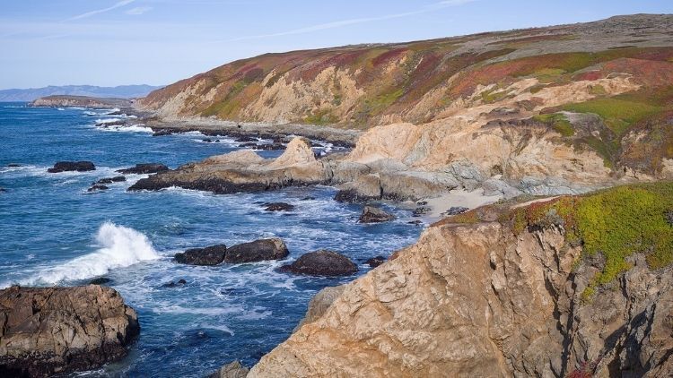 Rocky coastline along Sonoma County, California, with waves crashing against cliffs and colorful vegetation covering the hillsides. Rocky coastline along Sonoma County, California, with waves crashing against cliffs and colorful vegetation covering the hillsides.