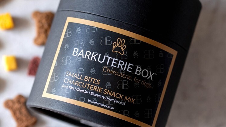 Container of BARKUTERIE Box dog treats labeled 'Small Bites Charcuterie Snack Mix' with colorful treats in the background. Container of BARKUTERIE Box dog treats labeled 'Small Bites Charcuterie Snack Mix' with colorful treats in the background.