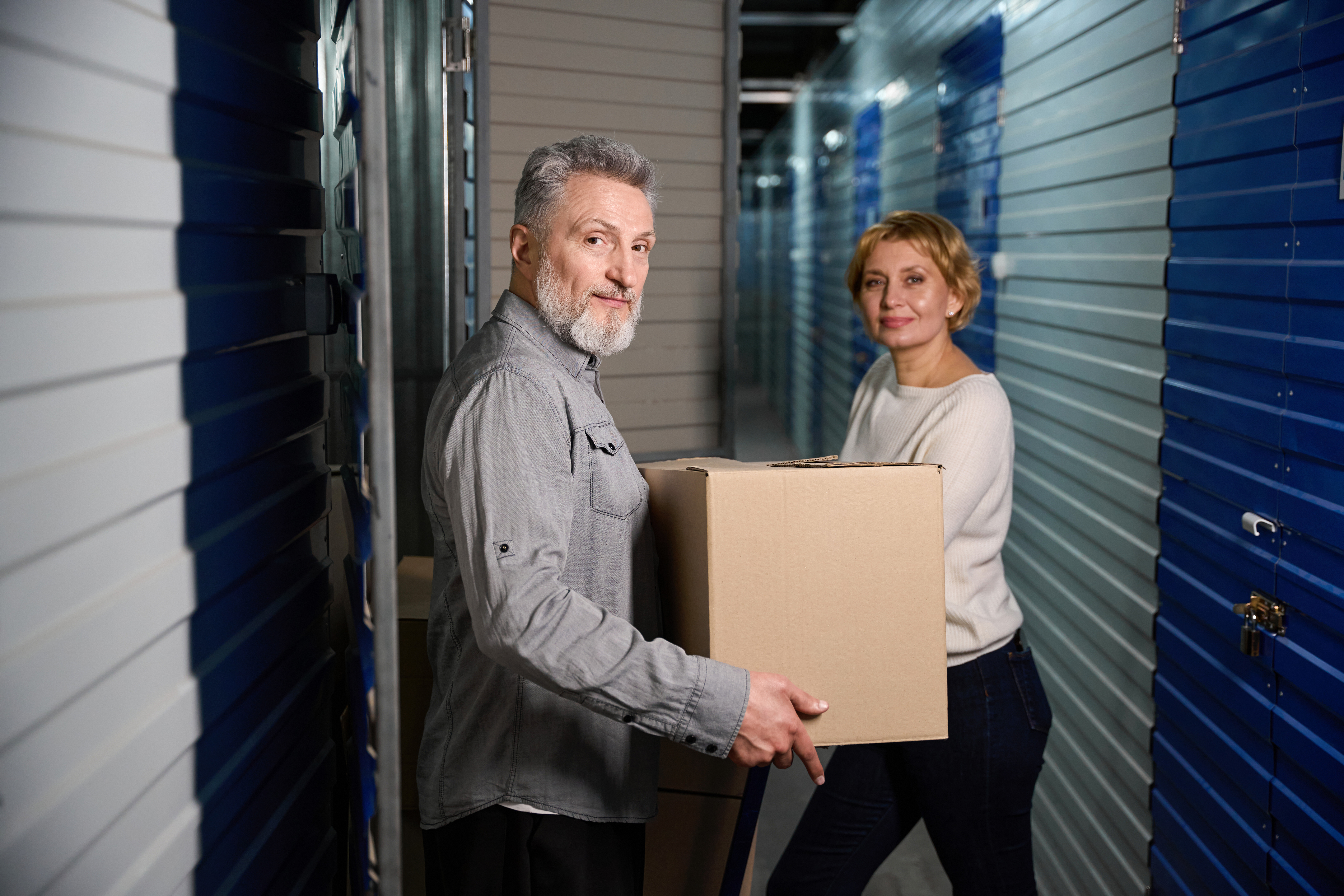 Couple placing a cardboard box inside a self-storage unit hallway. Couple placing a cardboard box inside a self-storage unit hallway.