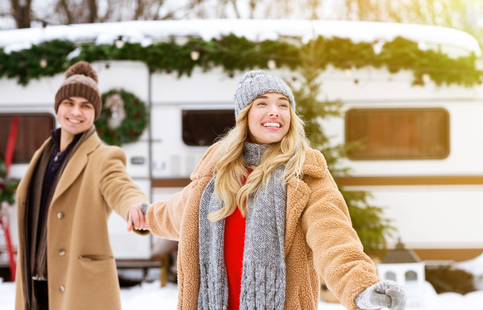 a young couple in front of their RV that is decorated with garlands in the snow