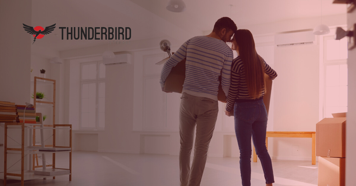 A couple smiling while carrying moving boxes in a bright, decluttered home, representing temporary storage options during a home sale with Thunderbird Storage.