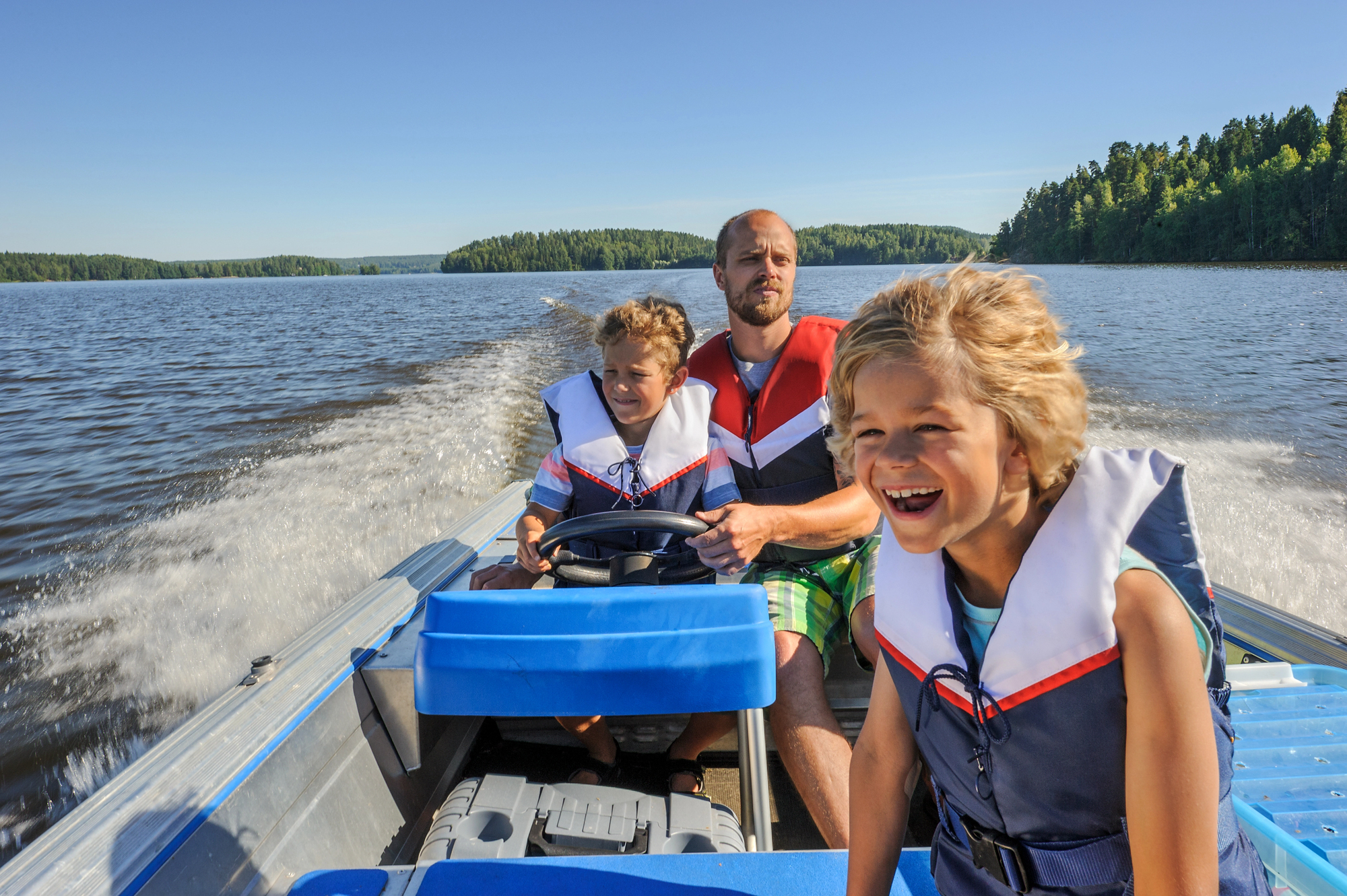 Father and two young sons laughing while going fast on a lake