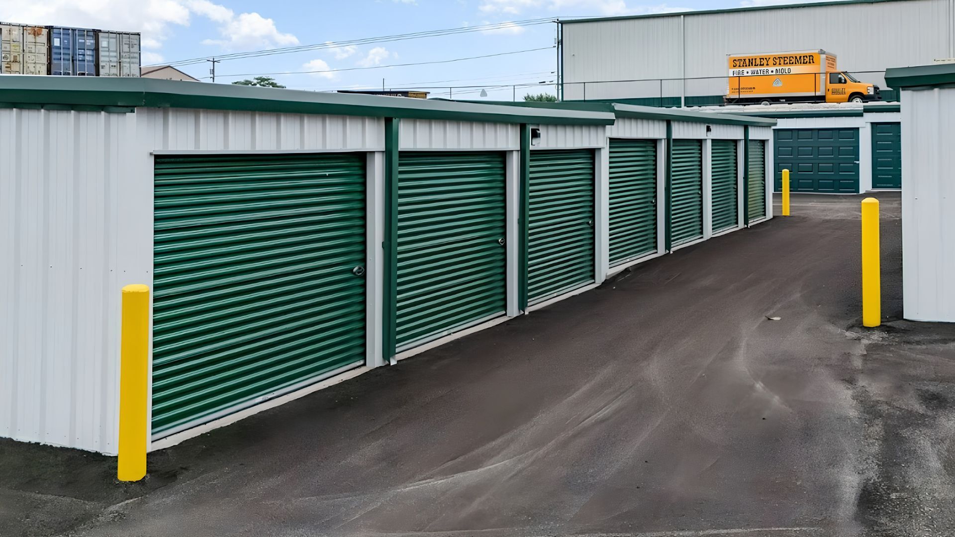 Driveway view of Hardin County Storage units with green doors, yellow bollards, and wide paved lanes