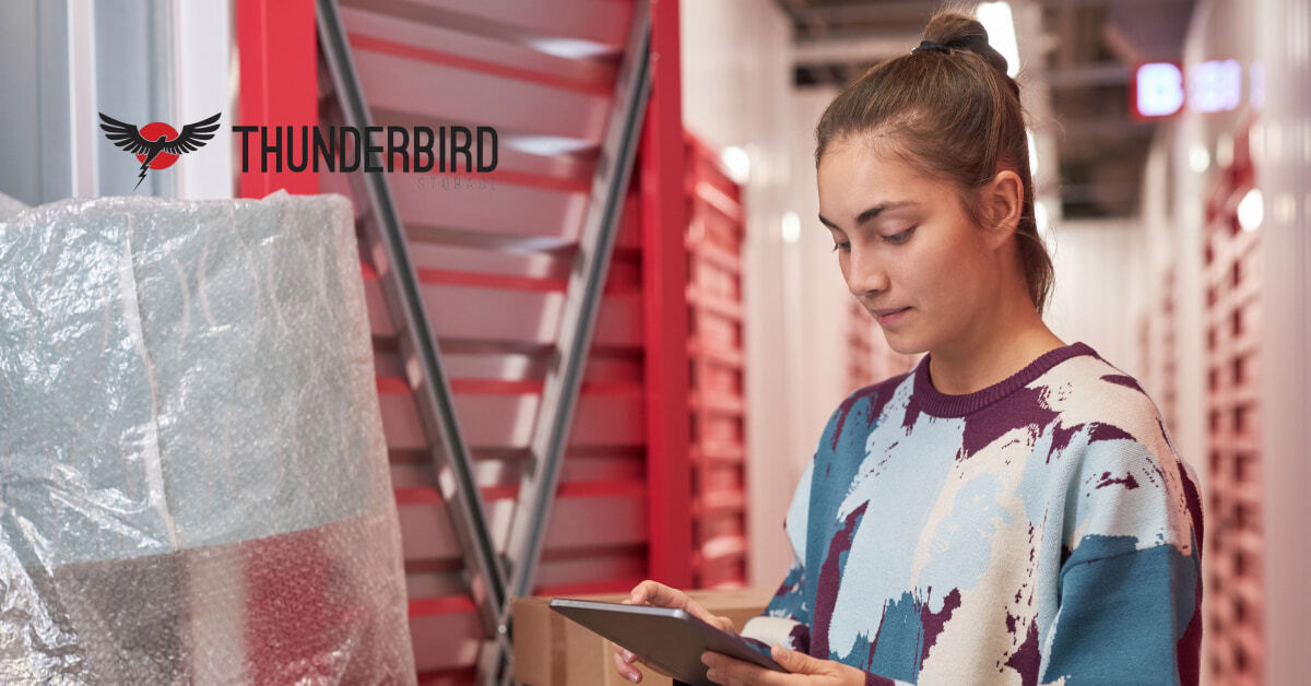 A college student using a tablet next to packed boxes and bubble-wrapped dorm items inside a clean Thunderbird Storage facility in Cedar City. A college student using a tablet next to packed boxes and bubble-wrapped dorm items inside a clean Thunderbird Storage facility in Cedar City.