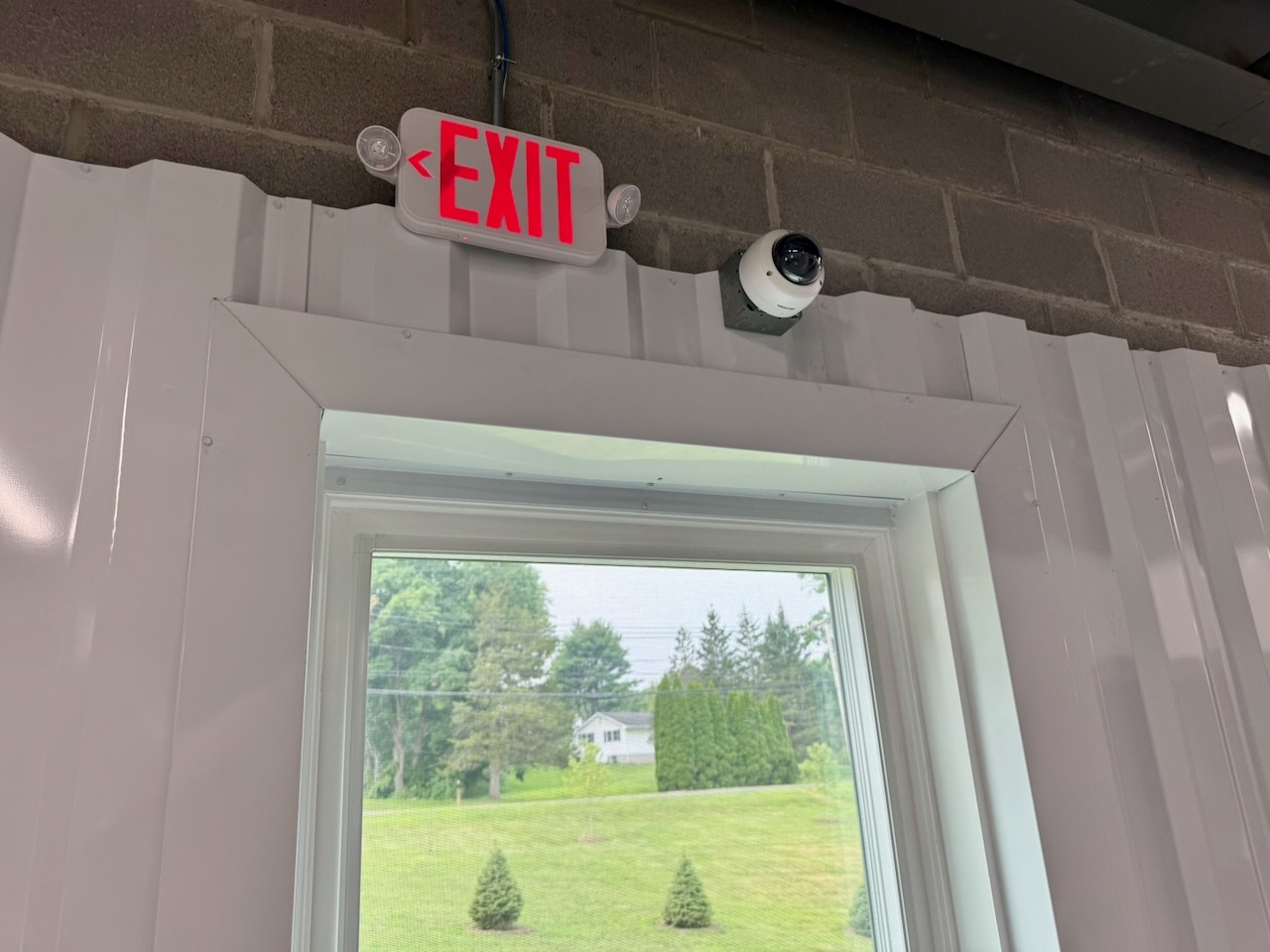 An illuminated emergency exit sign with backup lighting beside a dome security camera at Southbury Self Storage