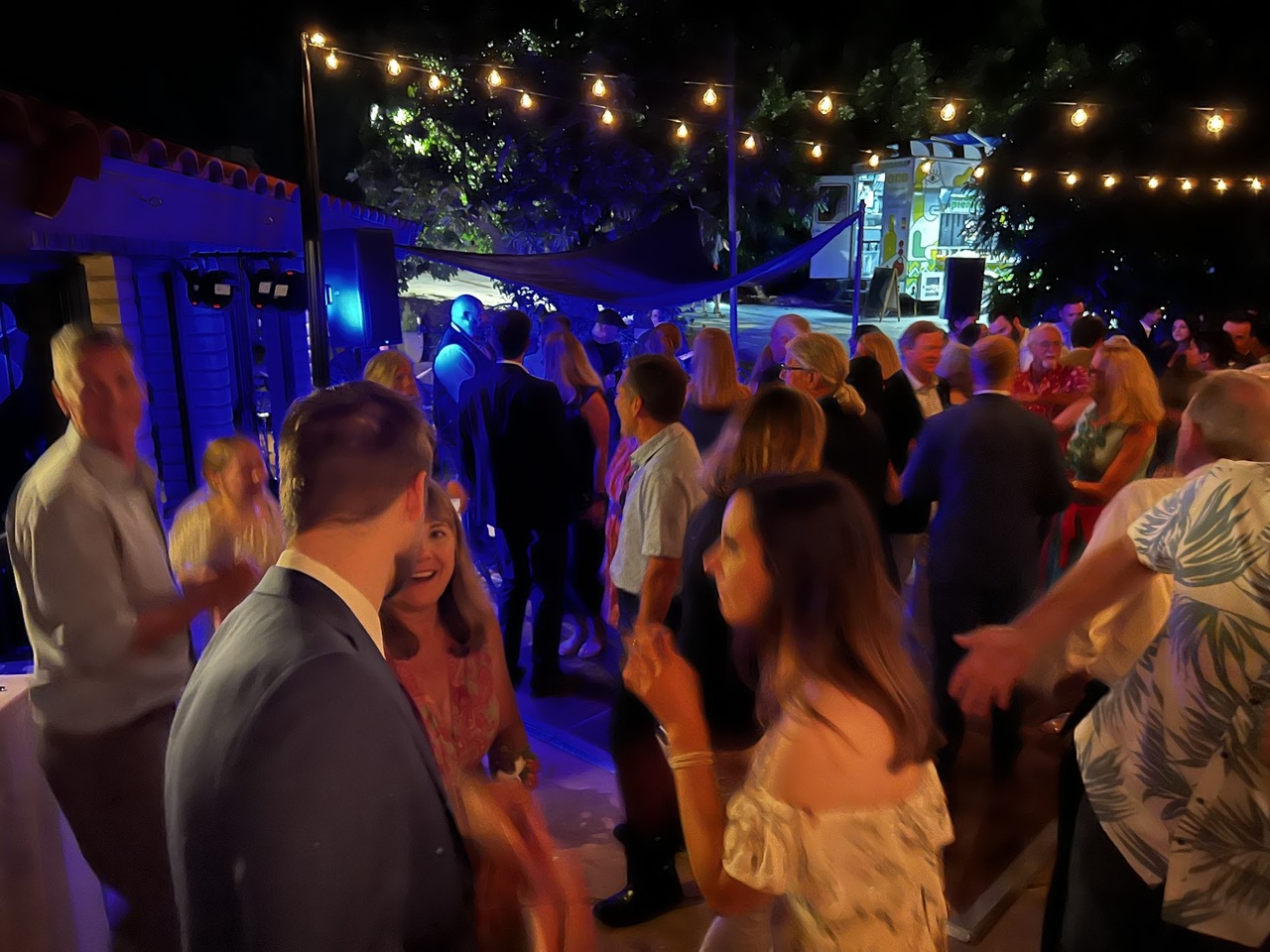 A crowded evening event under string lights in the Bridge courtyard