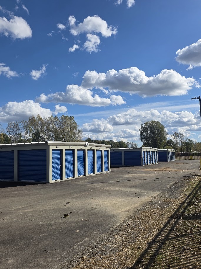 White storage buildings with blue doors along a paved drive at Handy Storage.