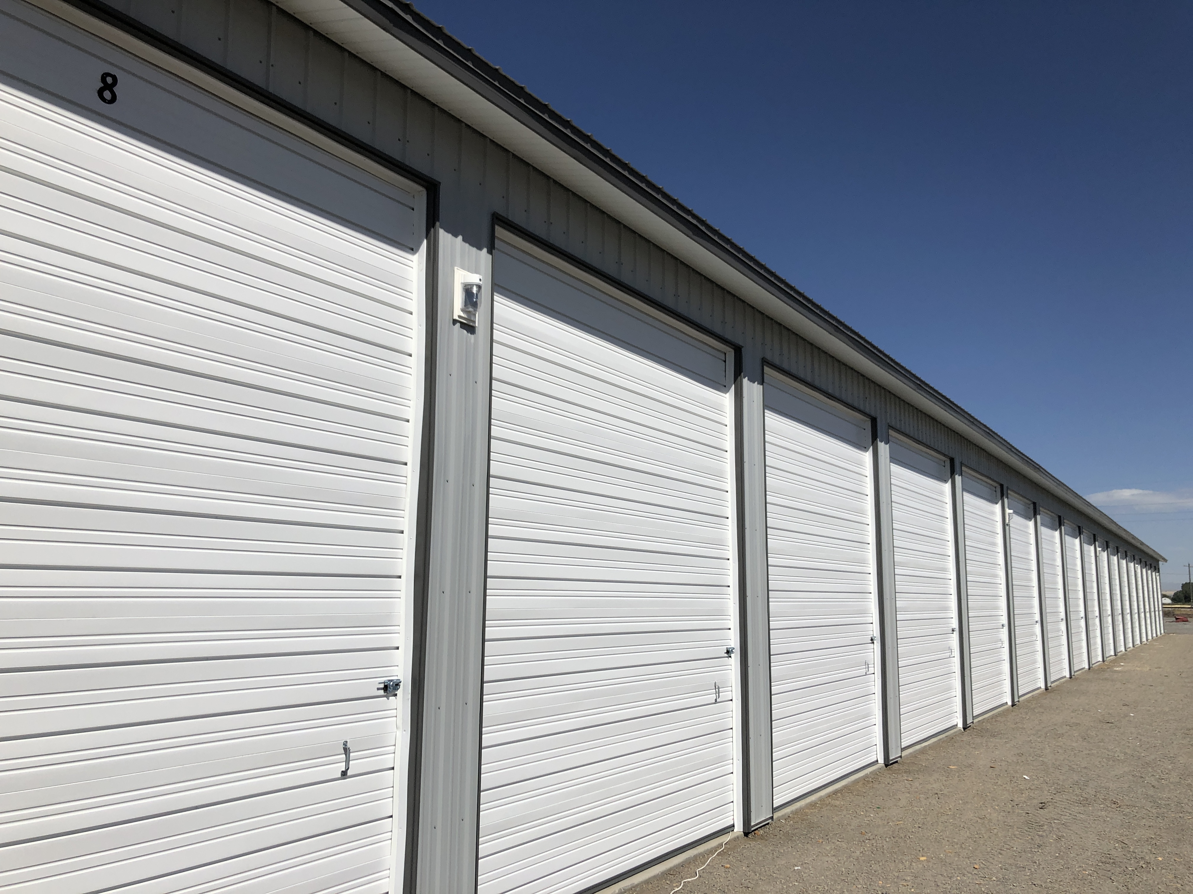 Row of enclosed drive-up storage units with white roll-up doors at Elite Storage in Rexburg, Idaho